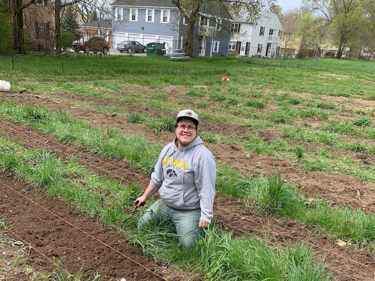 Finn Bell crouched down on the ground preparing soil for planting on a cloudy spring day