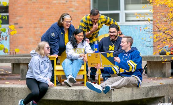 Group of students dressed in U-M gear looking at notebook by the Chancellor's Pond