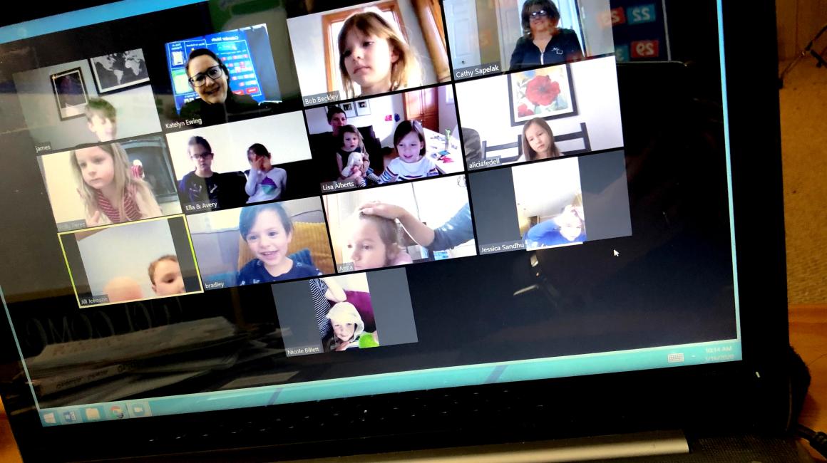 A photo of a laptop screen showing a Zoom meeting with a variety of kindergarten children and two teachers.