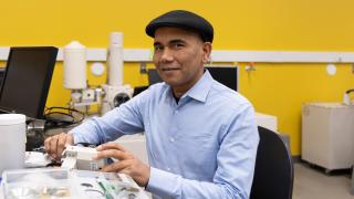 Wearing his signature black flat cap, UM-Dearborn Professor Pravansu Mohanty sits for a portrait in his UM-Dearborn mechanical engineering lab