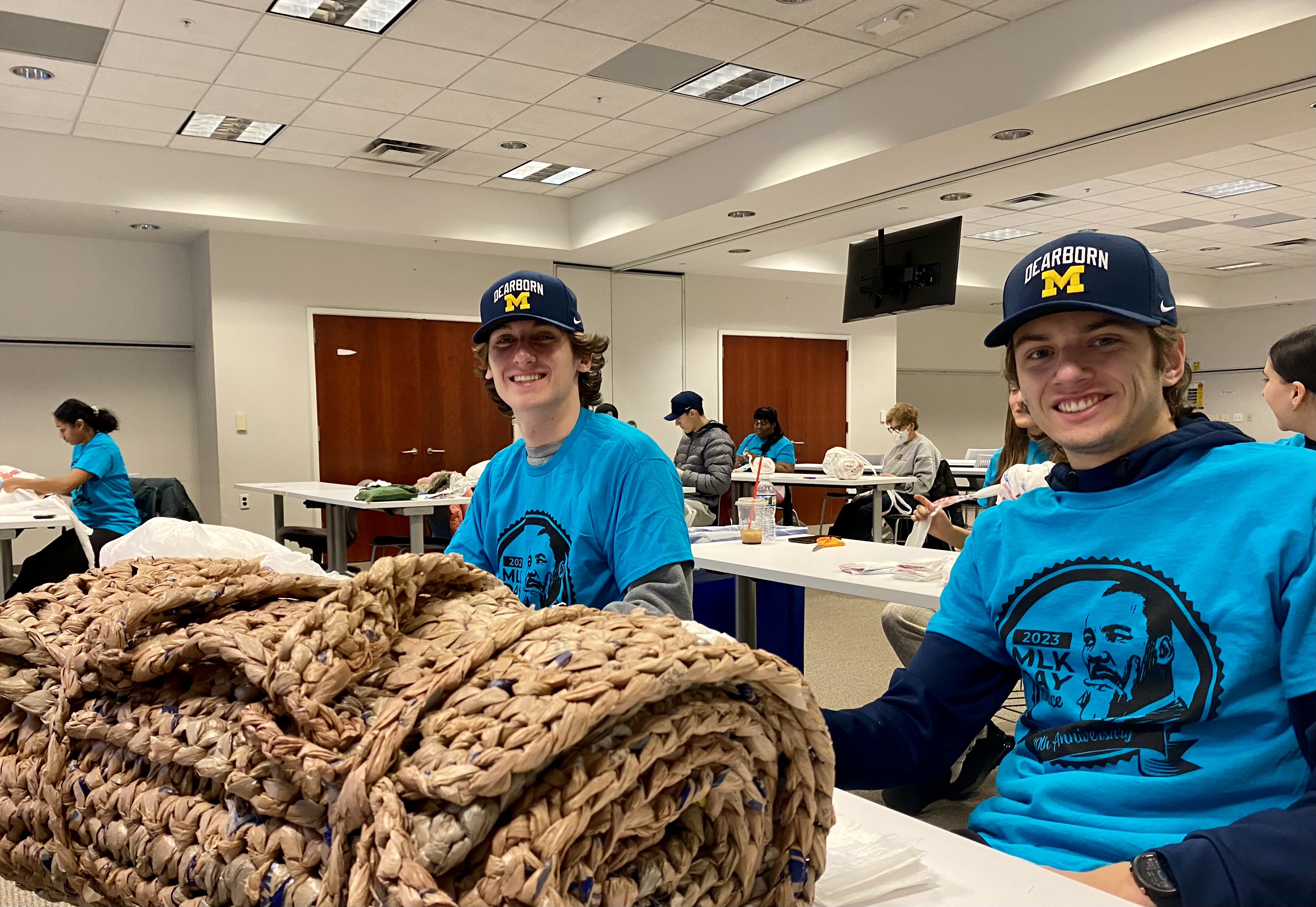 Photo of UM-Dearborn cross country runners Gavin Llewelyn and Luke Kaferle making rollable plastic mats with carrying handles for homeless shelters.