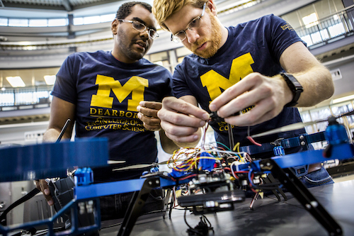 Two students wearing Michigan shirts work on an electrical controller.
