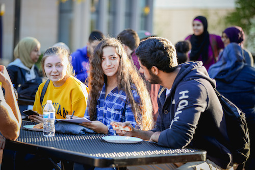 Students sitting a outdoor table talking and eating.