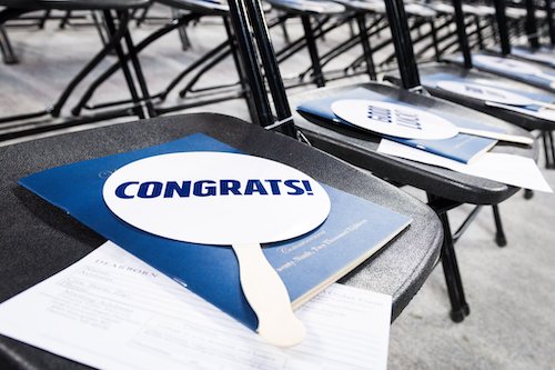  A row of chairs topped with commencement programs and handheld placards that say "Congrats" 