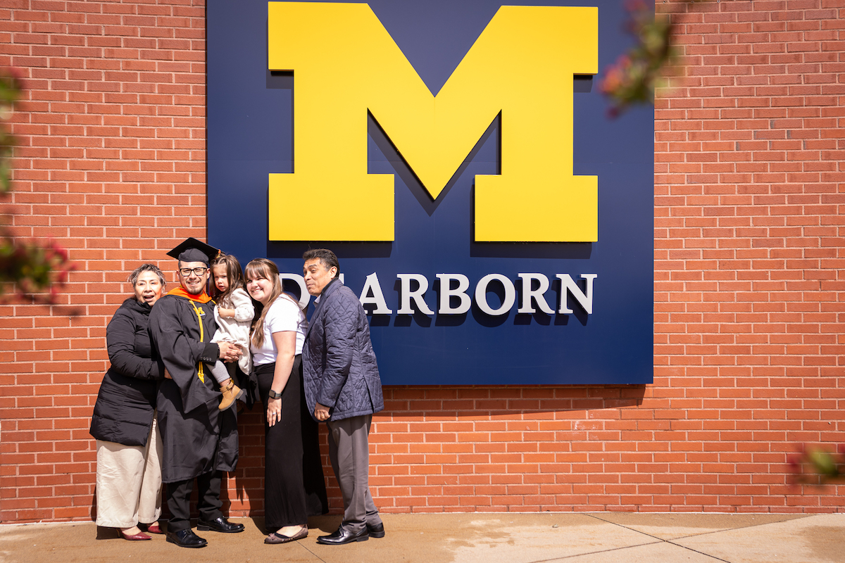 Graduate standing with family in front of UM-Dearborn block M