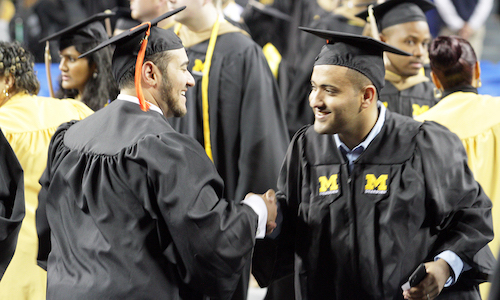 Two students shaking hands and congratulating each other at commencement.