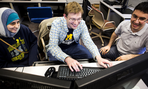 Three students working around a computer.