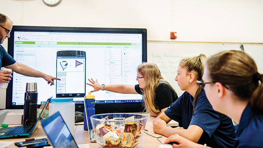   Coding instructor Josh Rychlicki (left) and UM-Dearborn student Jessica Sterly (center) help camp participants review the visual interface design they came up with for a golf app.