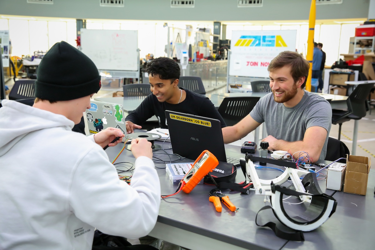 3 students working in Engineering lab working on computers and robots