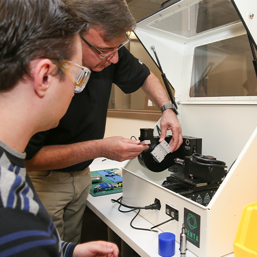 Two individuals examining equipment in a lab setting, with one adjusting a device as the other observes.