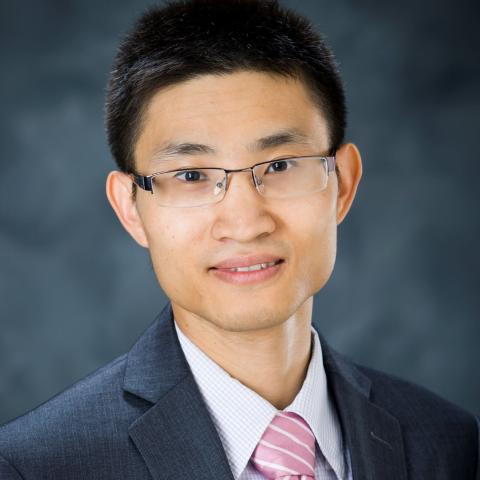 Portrait of a professional wearing glasses, a gray suit, and a pink tie.