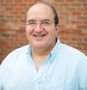Photo of a man in a blue shirt with a brick wall in the background