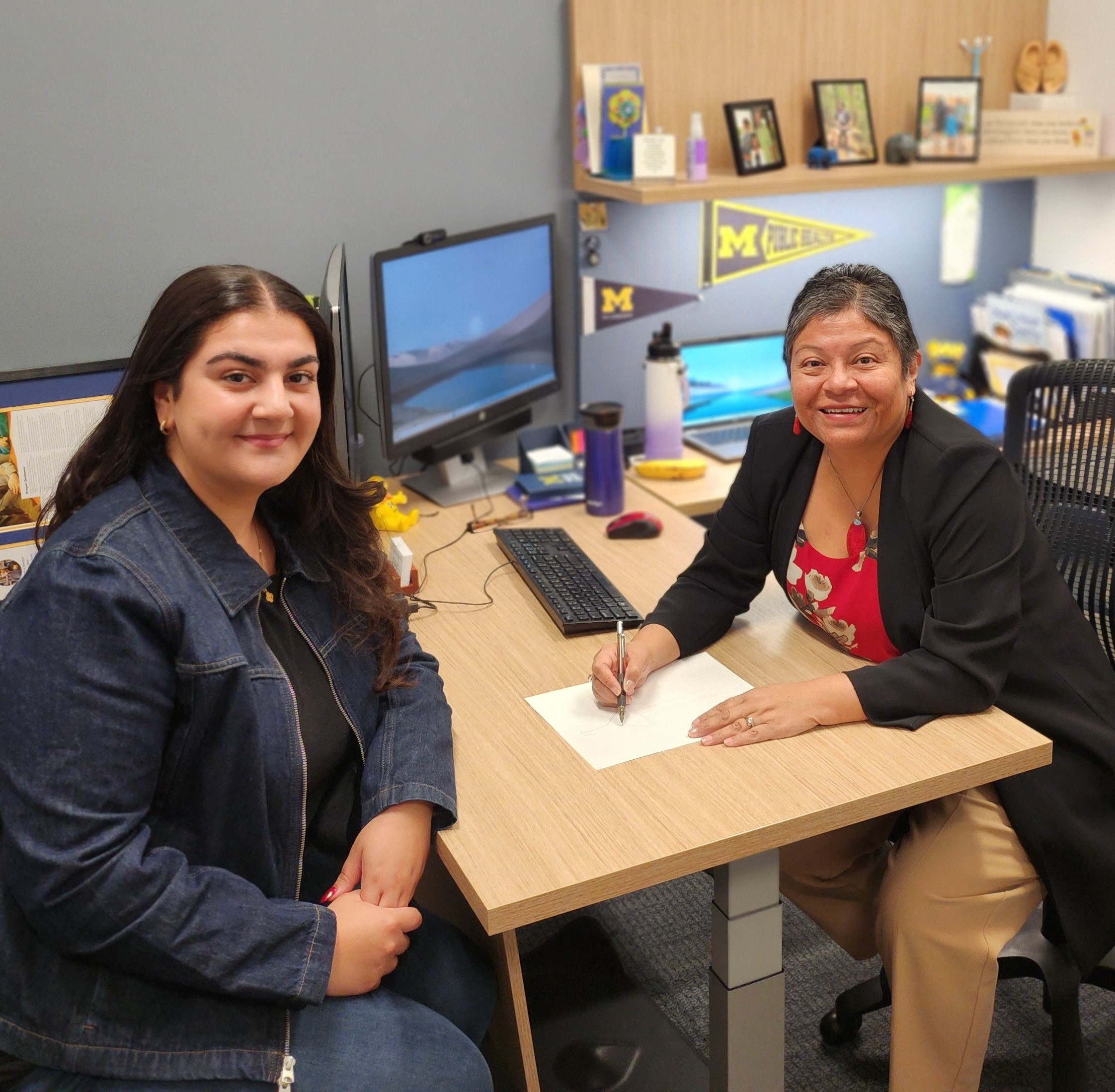 Student and Staff at desk smiling at camera.