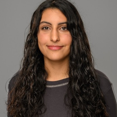 Photo of a smiling young female who with long dark hair. She is wearing a gray and black top.