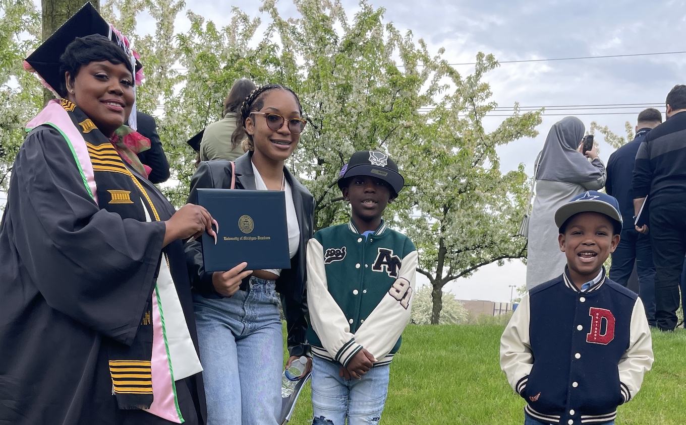 A woman holding a diploma stands with her three children, ages 17, 8 and 9