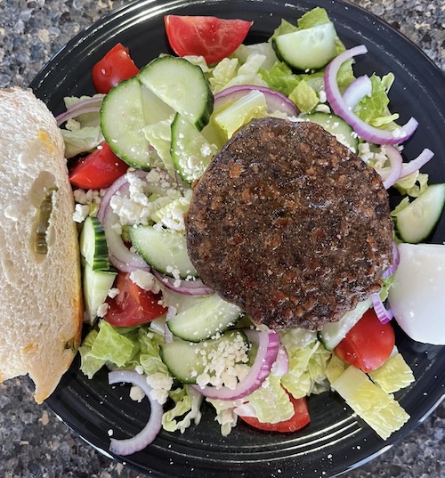 A photo of a round burger patty on top of a salad of lettuce, tomatoes and red onions