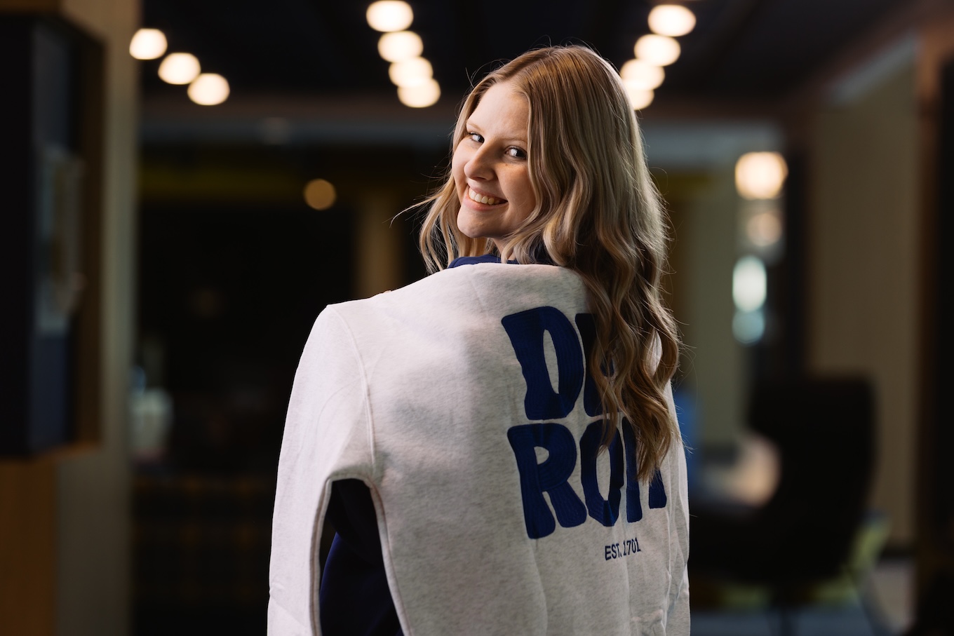 A woman wears a gray sweatshirt with blue embroidered letters that say "Detroit."