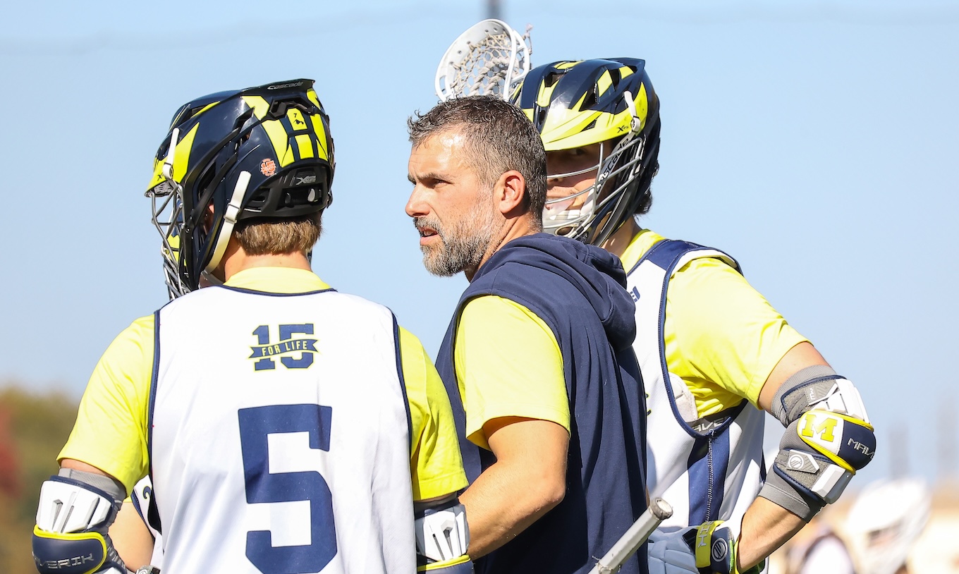 Two male lacrosse players from UM-Dearborn's team stand near the team's coach.