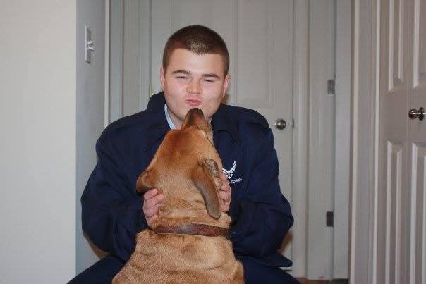 A man wearing an Air Force uniform is greeted by his dog following his return home on leave.