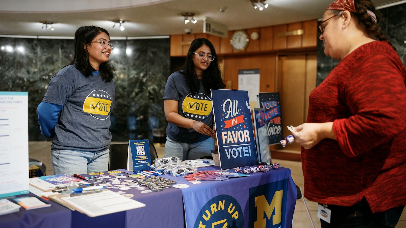 Two female students talk about voting to a female Dearborn community member.