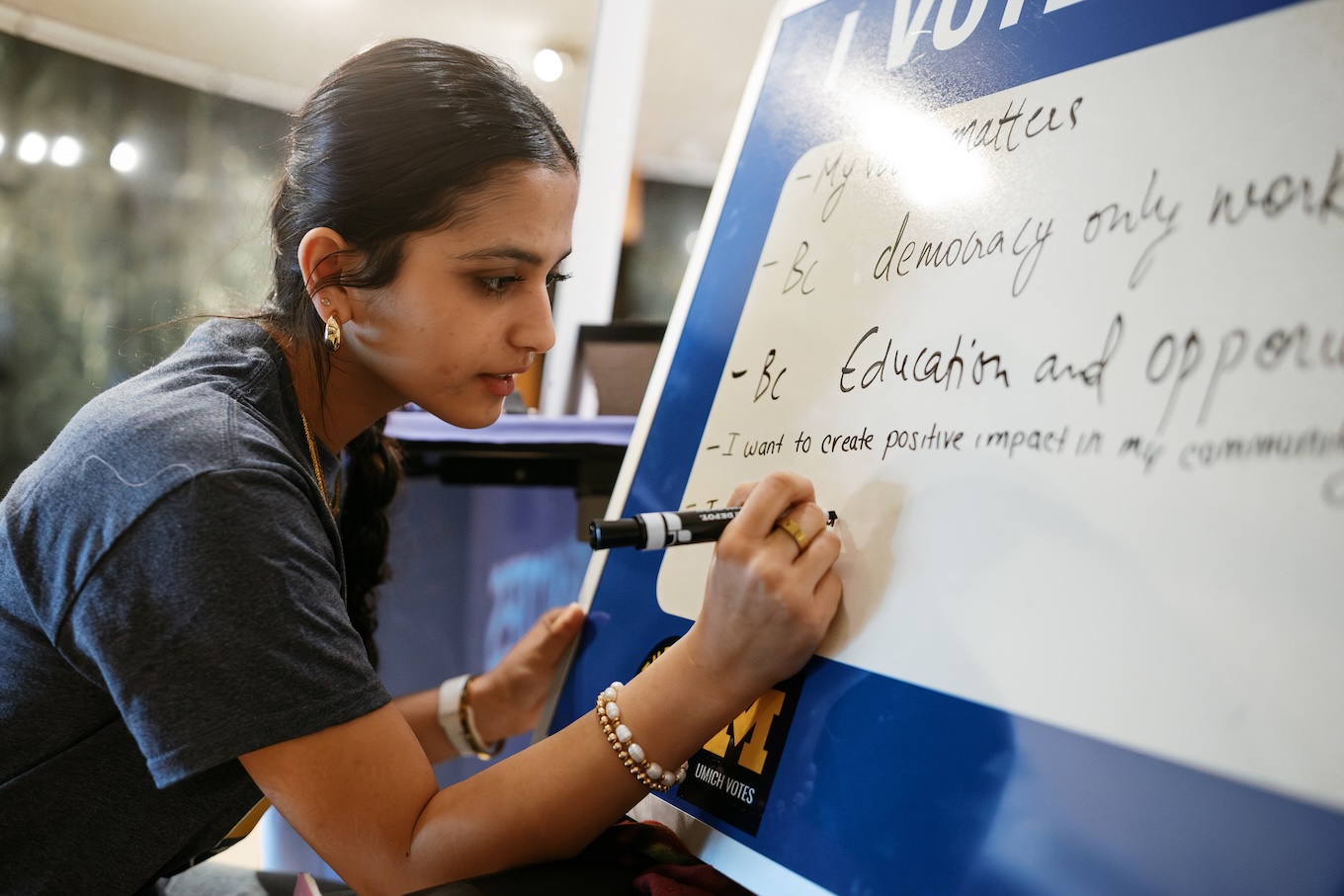A young woman uses a blue marker to write sentences on why she wants to vote