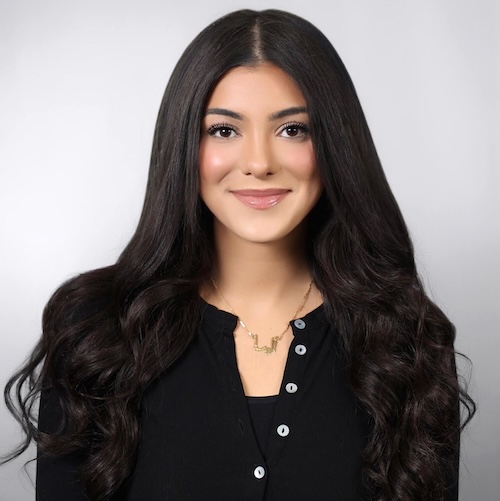 Portrait of a young woman with long black hair, who is wearing a gold necklace and a black dress