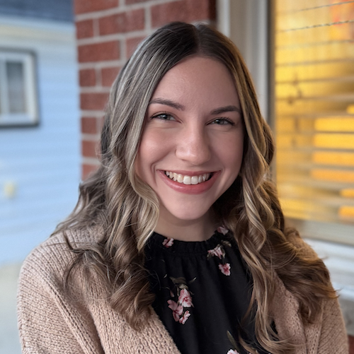 A smiling woman wears a beige jacket in a portrait