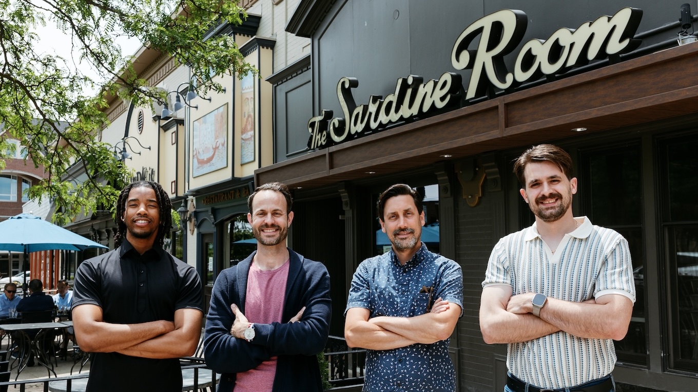 Four men in business casual clothing stand in front of a restaurant with a sign that reads, "The Sardine Room."