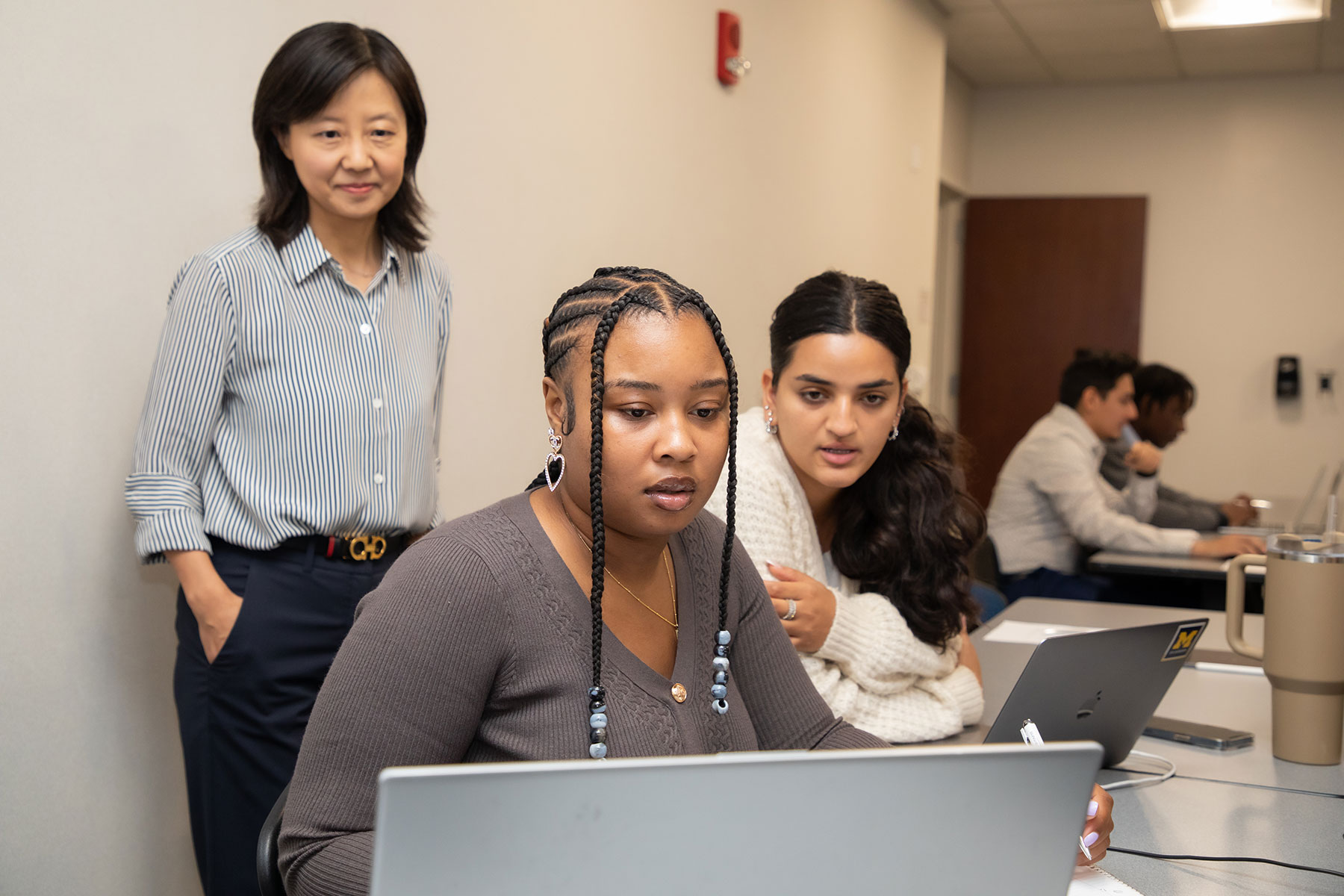 Two UM-Dearborn College of Business students and a professor looking inquisitively at a laptop.