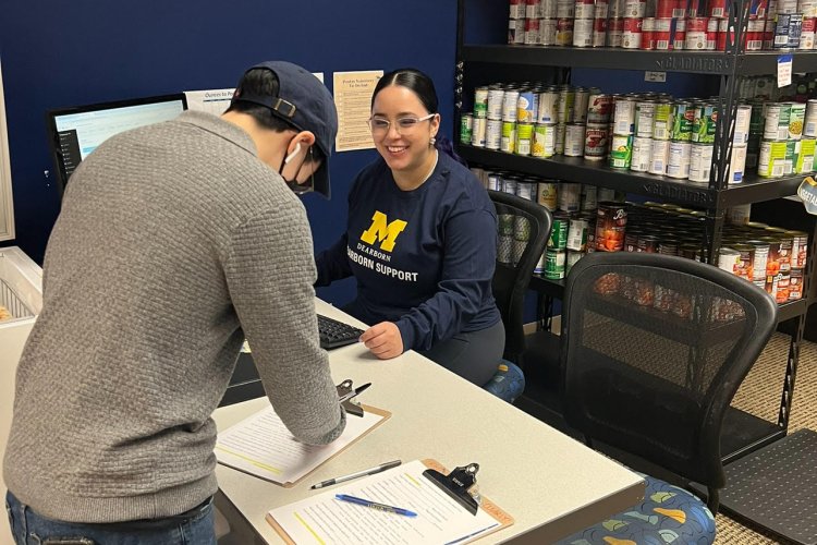 A smiling person wearing a block M shirt helping a student