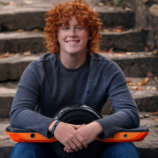 Person with red curly hair wearing a blue shirt sitting on stairs outside.