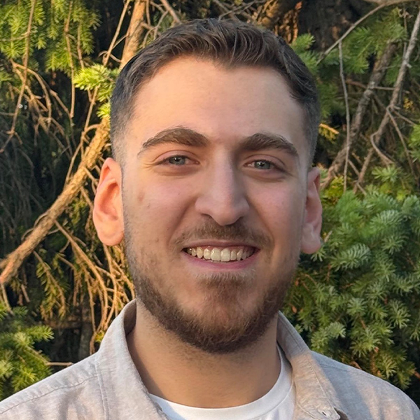 Person with short hair smiling against a green background.