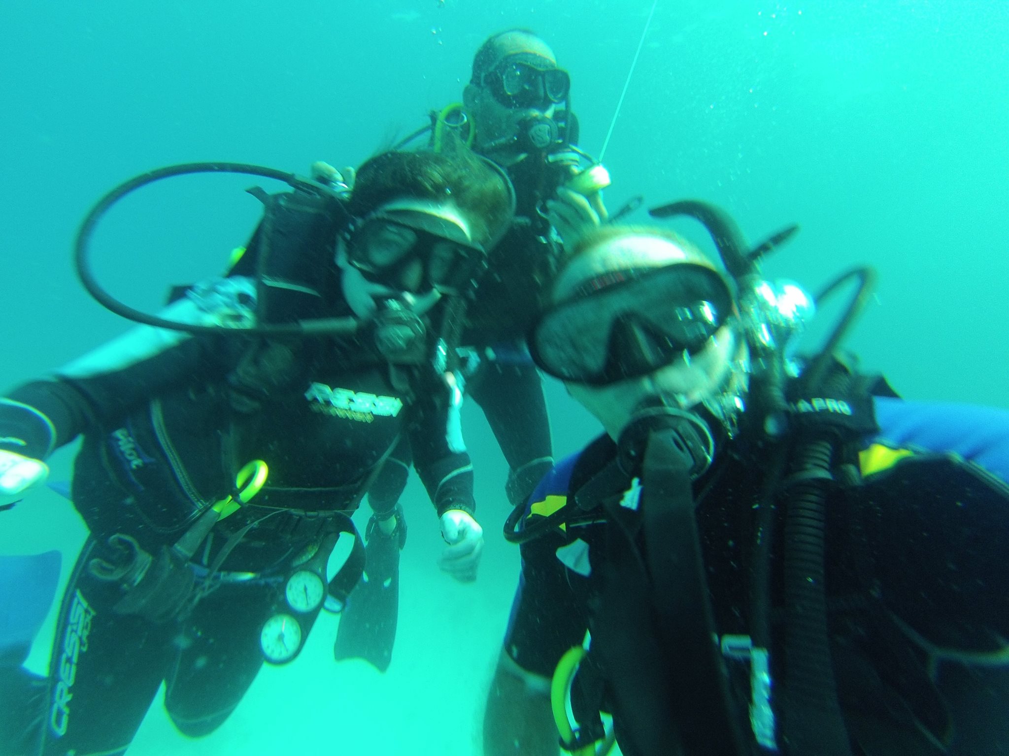 Three students in a selfie underwater. They are wearing scuba diving gear.