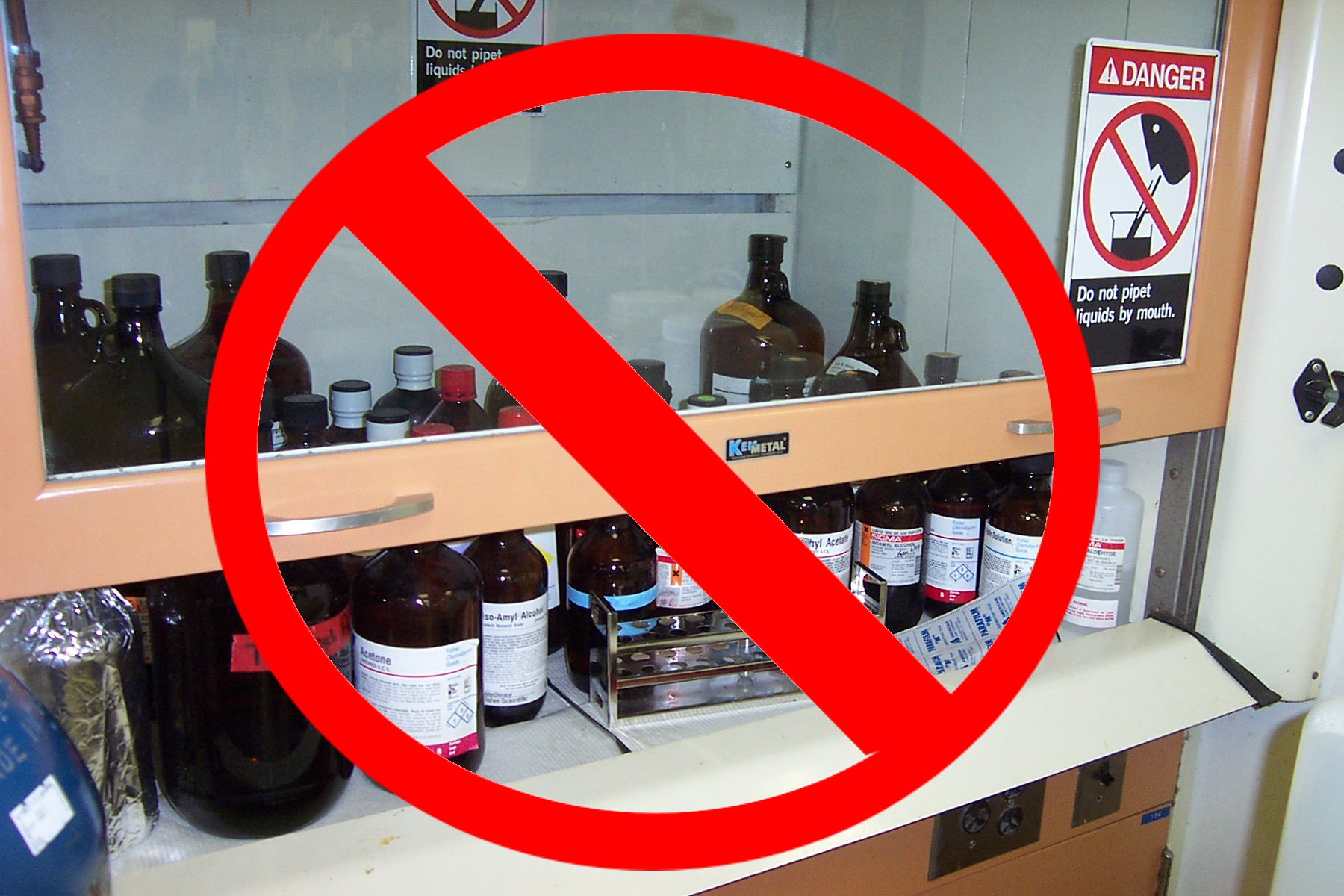 Many bottles of chemicals stored under fume hood with red circle and line through it.