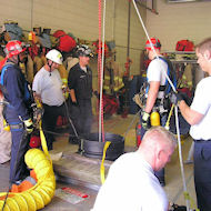 Group of people wearing hard hats standing around small confined space with ropes