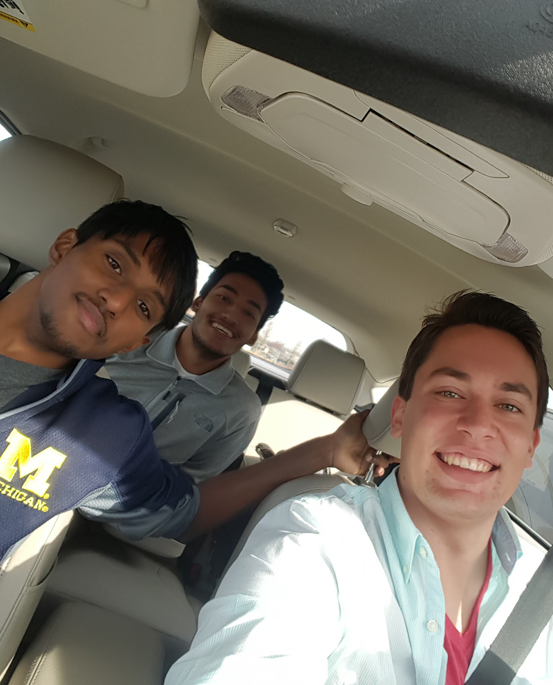 Three male students sitting in a car with a beige interior as part of a car-sharing study
