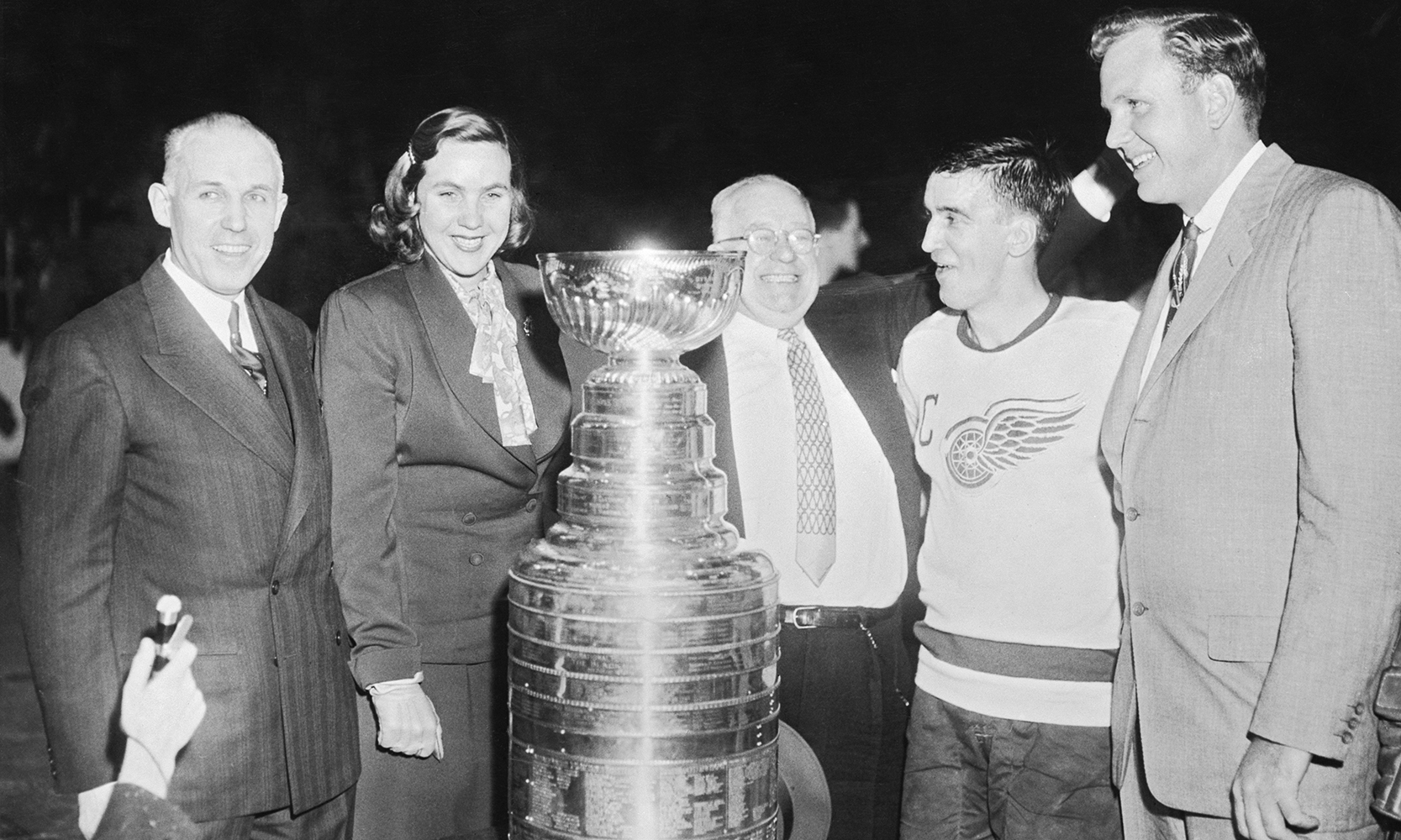 Detroit Red Wing player standing with 3 other men and 1 woman next to the Stanley Cup