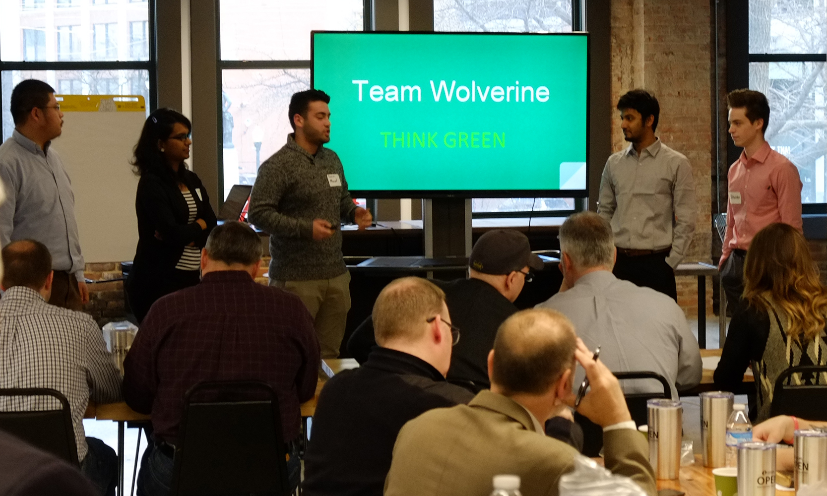 Presentation of 5 people in front of a screen that reads: Team Wolverine Think Green.