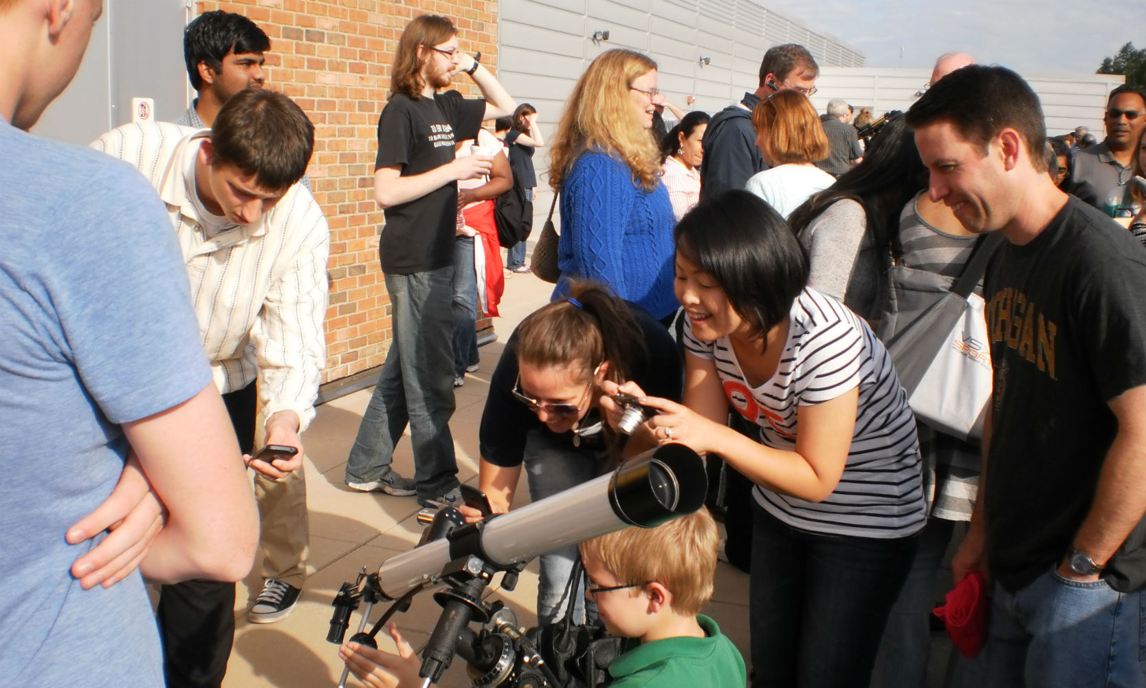 Public observation at the Observatory. Parents and children gather around a telescope outside.