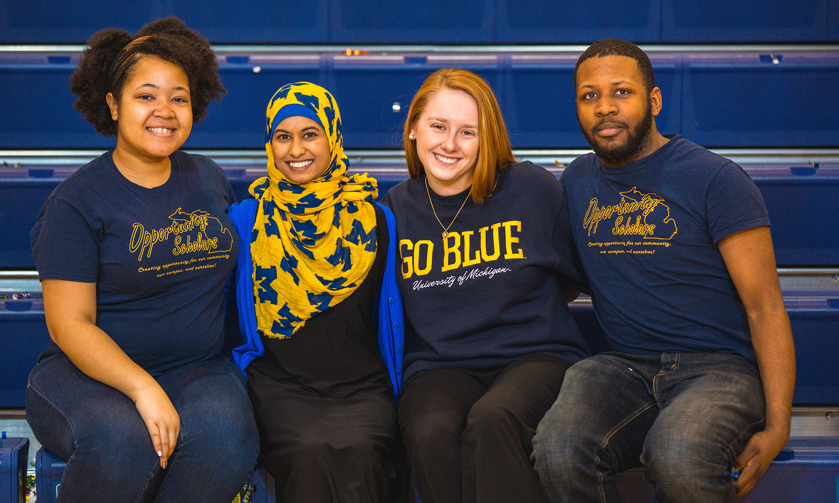 4 students sitting arm in arm with UM-Dearborn attire.