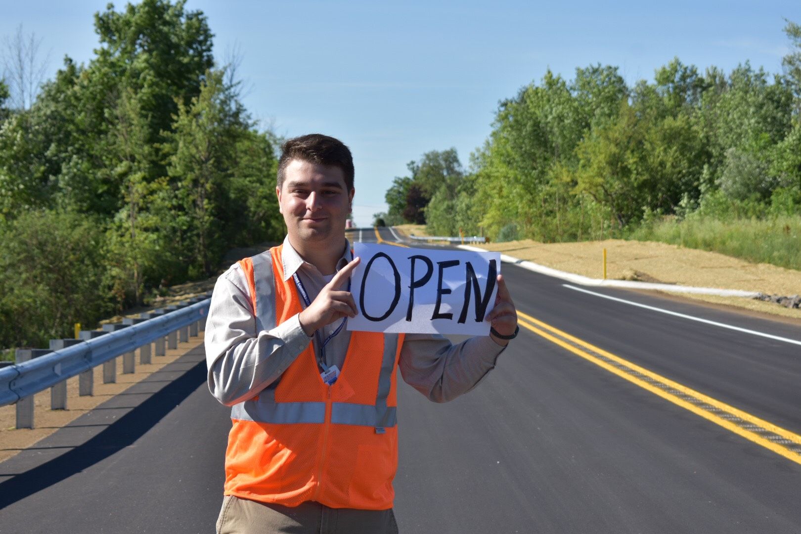 Jack VanAssche standing on road with orange safety vest holding a sign that reads: open.