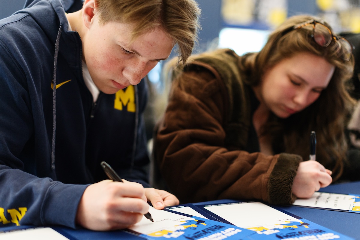 Two students, a male and a female, write messages to donors in thank you cards