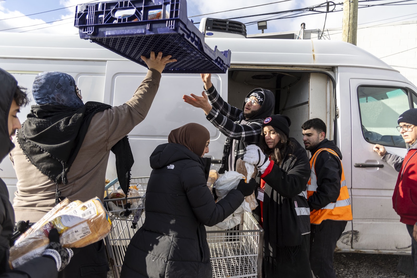 People lift a crate of food into the air to pack it into a van.
