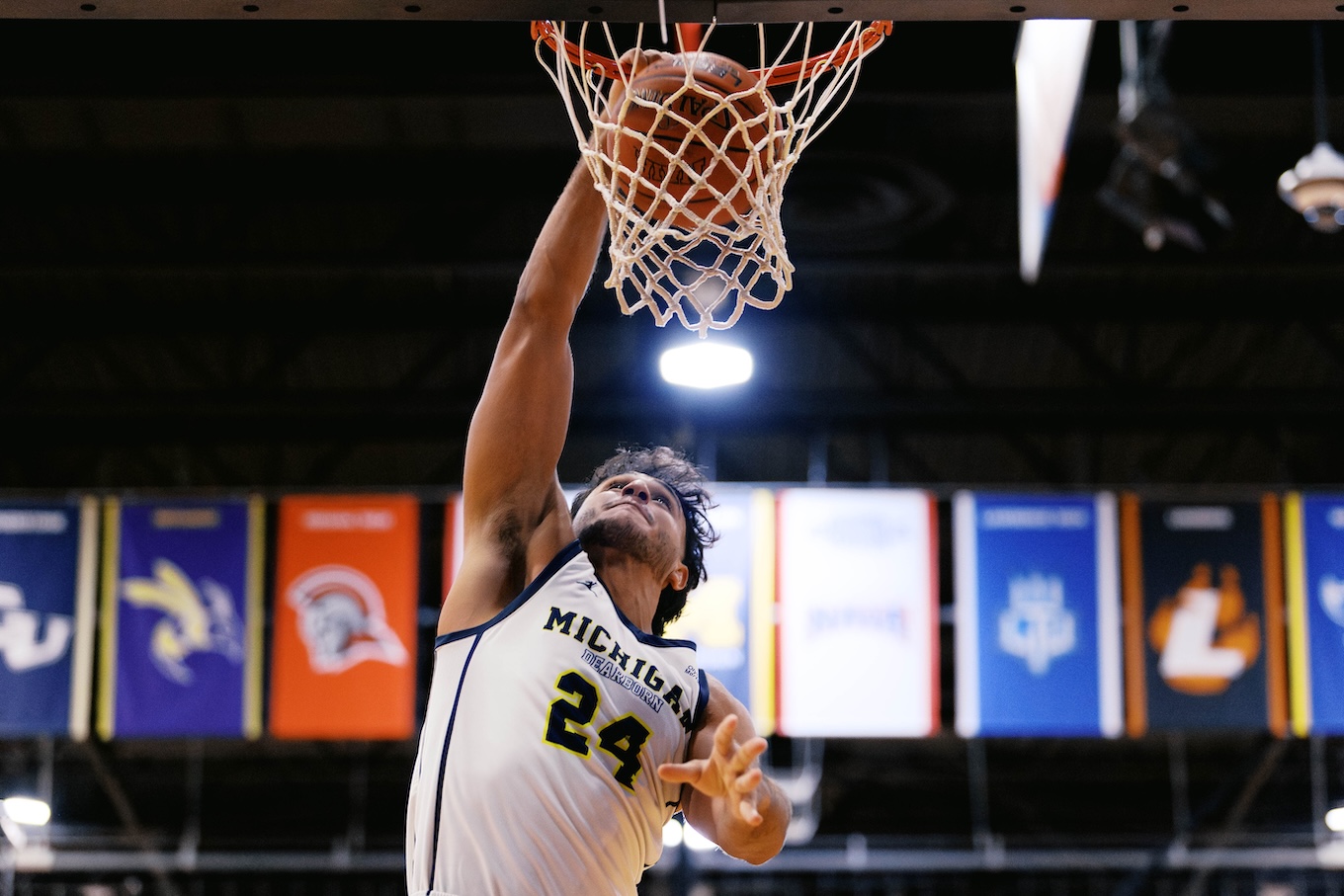 A male basketball player jumps up to a basketball rim and puts the ball in.