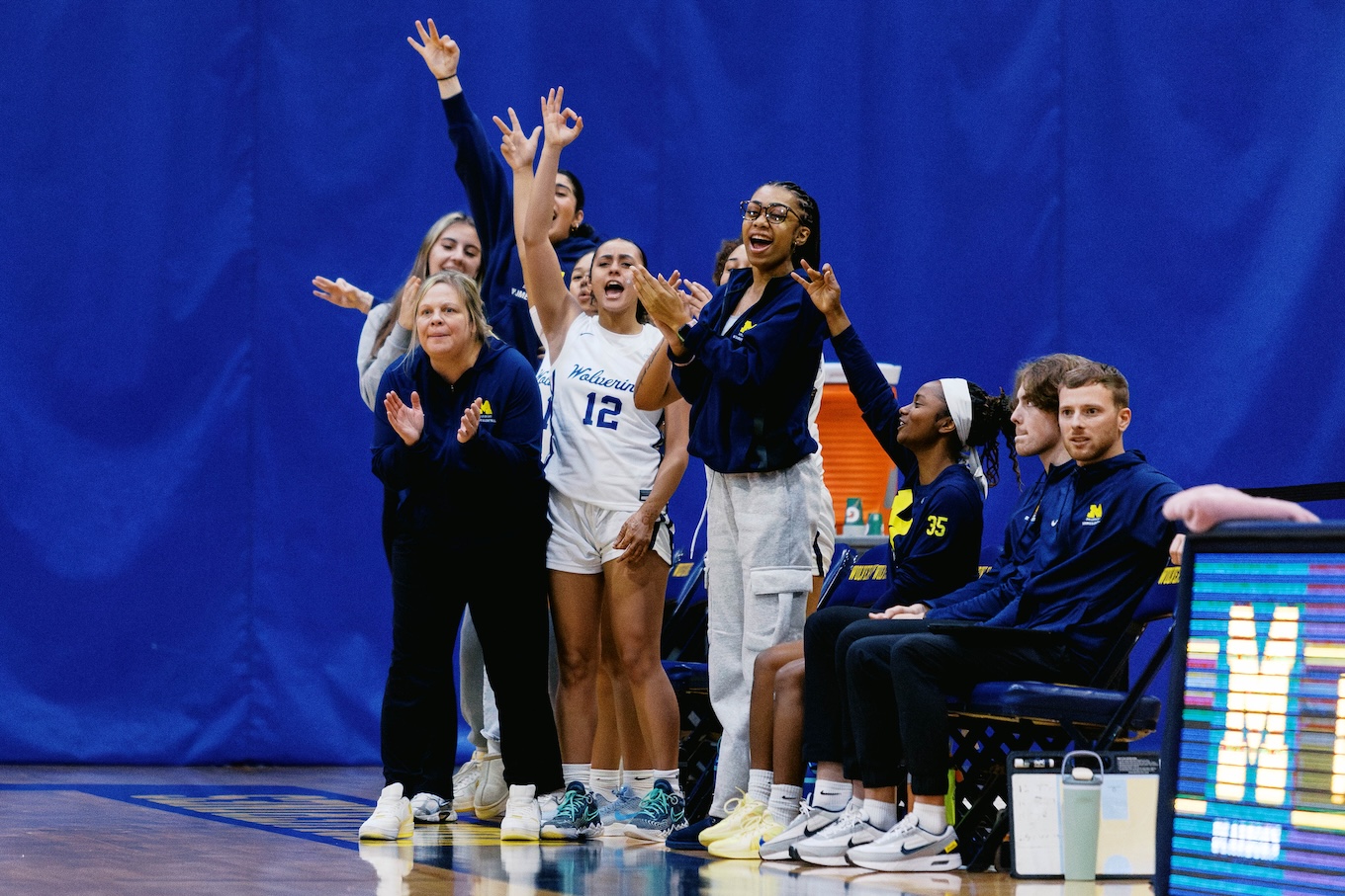 A group of female basketball players cheer on their team from the side of the court.