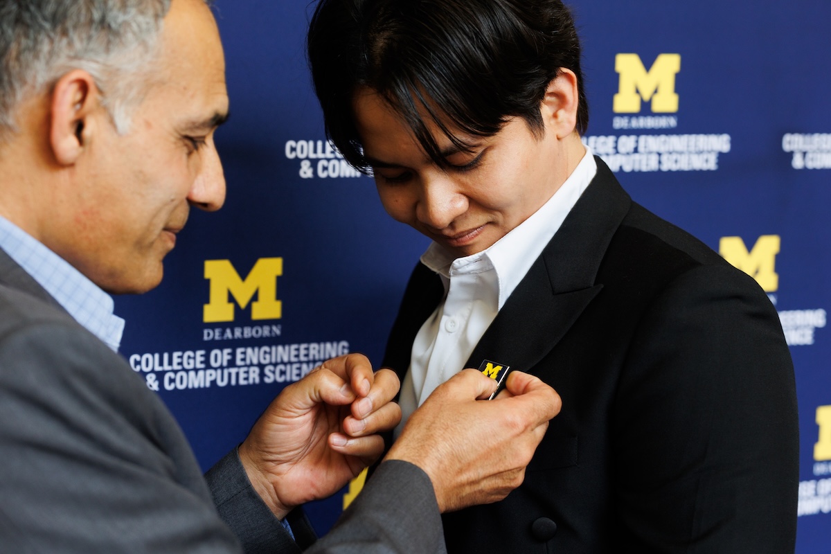 Two males stand together and one places a UM-Dearborn on the other's suit jacket