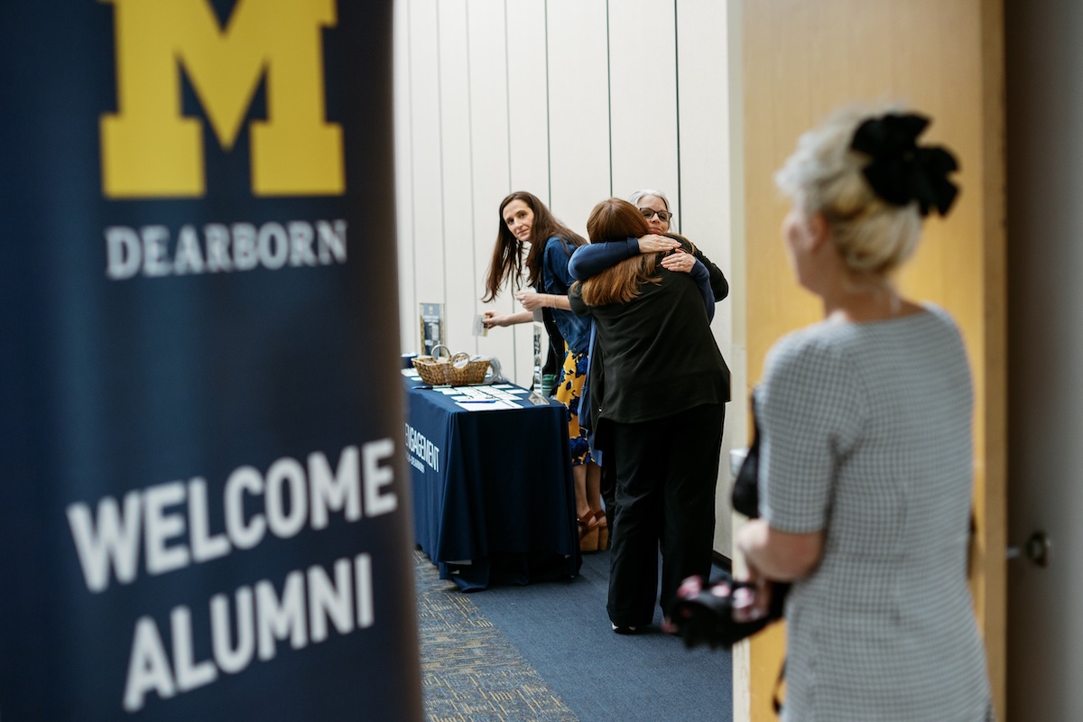 Two women hug inside of a doorway. They are entering a room for a lunch meeting.