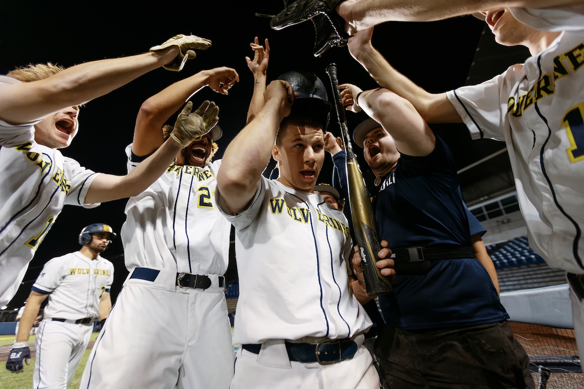 Baseball team players gather on the field to celebrate with their bats and gloves.