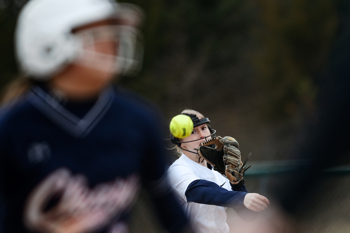 A woman softball player catches a yellow softball in her mitt.