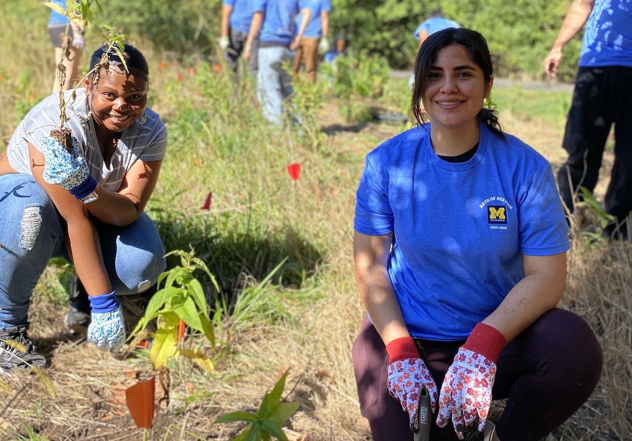 Two students plant native leafy plants on the university grounds.